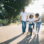 An image of a family teaching their child how to ride a bike, symbolic of them teaching them all the steps of growing up, including helping them with financial planning and saving by giving her pocket money.